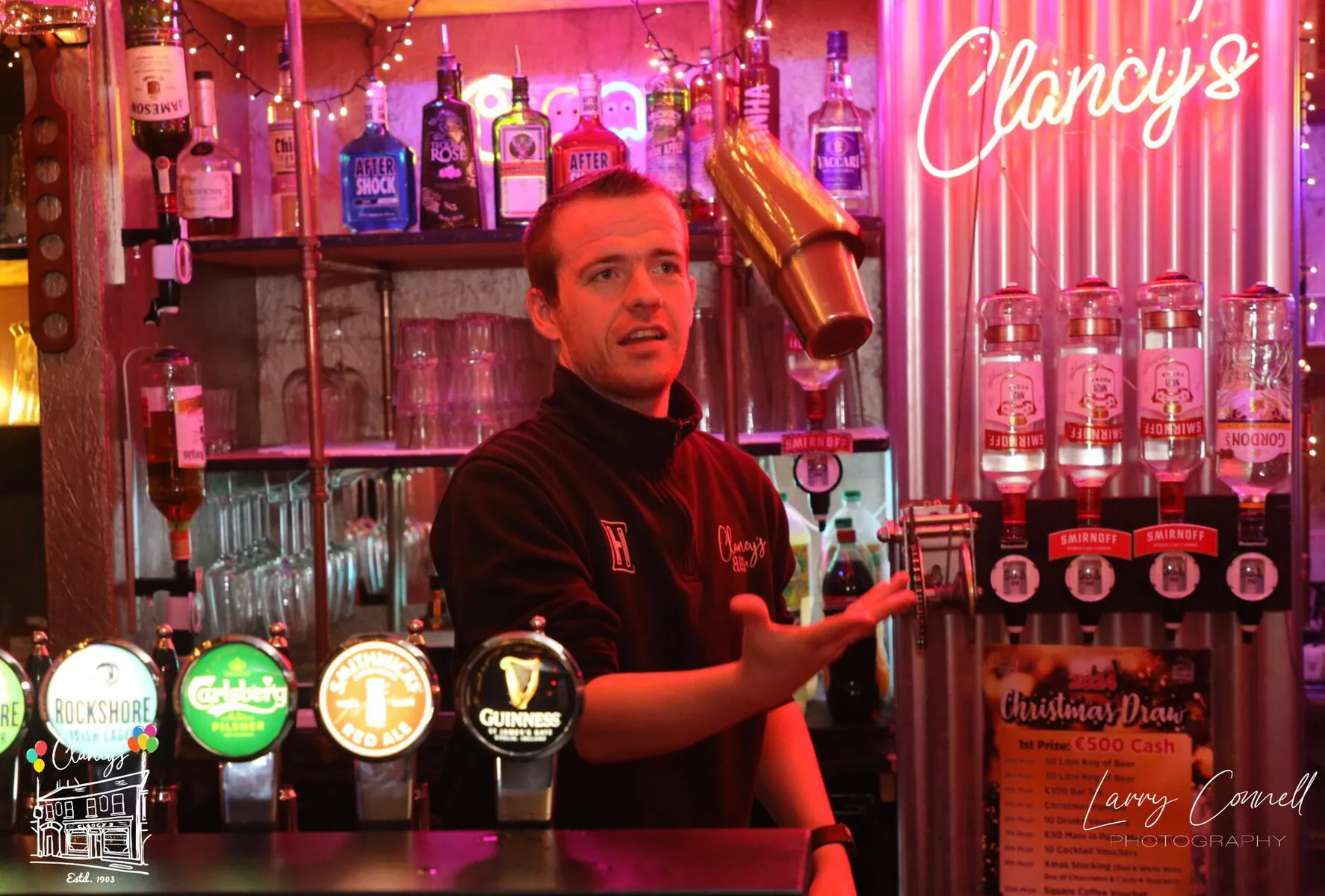 Clancy's bartender flipping a cocktail shaker behind the neon-lit bar