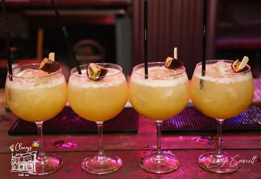 A line of four signature cocktails on the bar at Clancy's, garnished and lit by neon